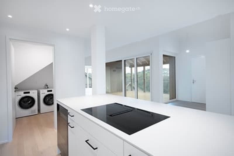 Modern kitchen with white cabinets, induction cooktop, and a washing machine in the background.