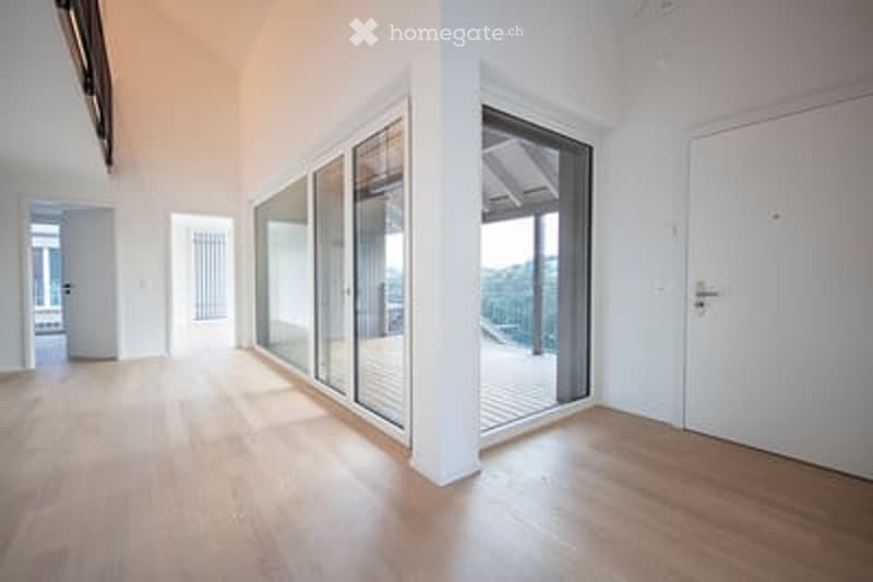 Bright, unfurnished room with large glass sliding doors leading to a balcony, wooden flooring, and white walls.