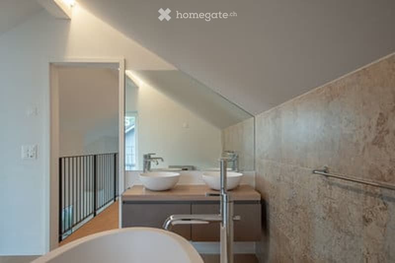 Modern bathroom with a double sink vanity, sleek faucets, a bathtub, and a large mirror. The space features clean lines and contemporary design elements.