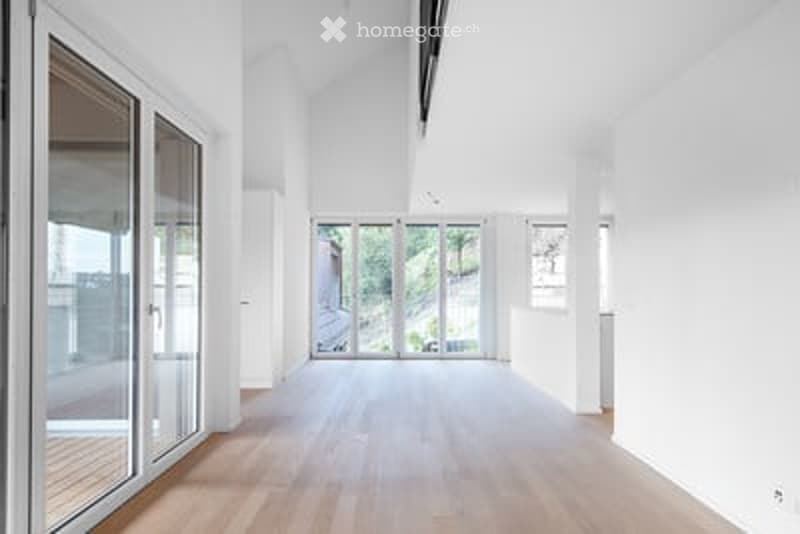 Bright, empty room with wooden flooring, large glass doors leading to an outdoor area, and white walls.