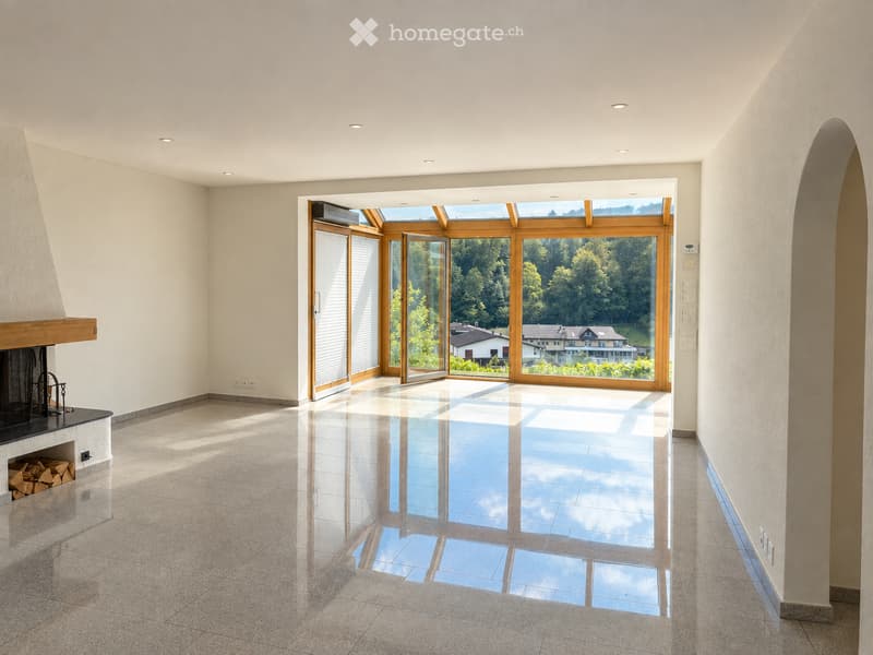 Bright, empty room with polished tile flooring, large sliding glass doors opening to a scenic view, and a built-in fireplace with stacked firewood.