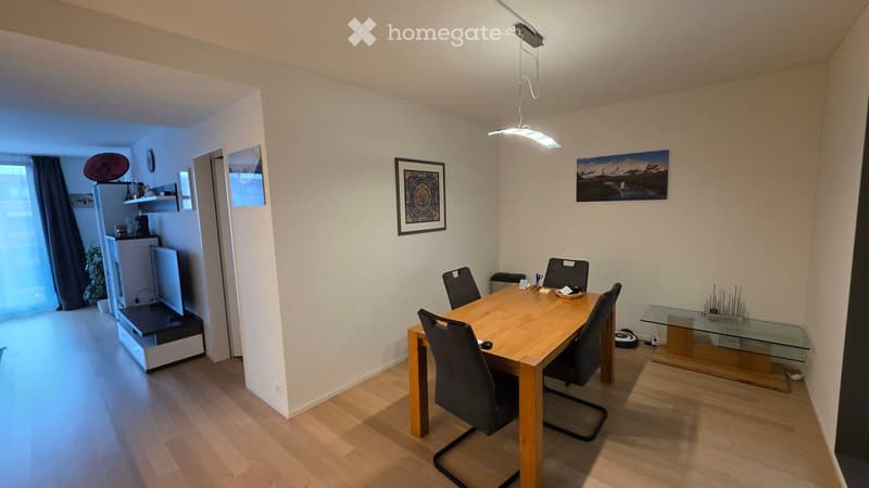 Dining room with a wooden dining table and chairs, a glass side table, a refrigerator, and a TV in the adjacent living area.