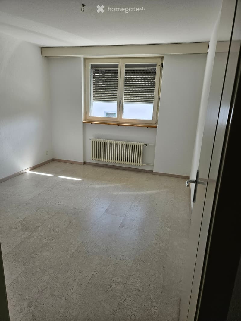Empty room with tiled floor, white walls, a window with blinds, and a radiator below the window.
