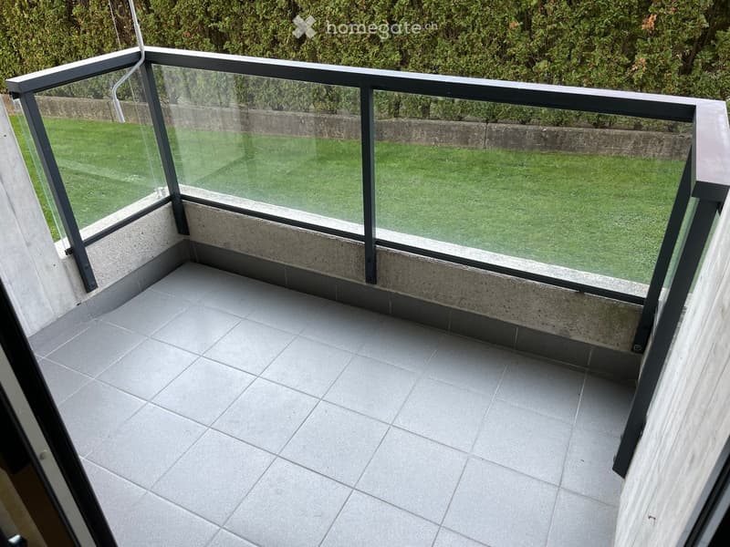 Balcony with glass railings, tiled floor, view of a grassy lawn