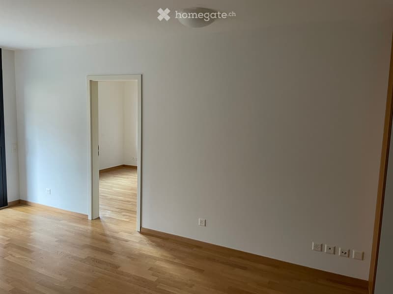 Empty room with white walls, wooden floor, and a door leading to another room.