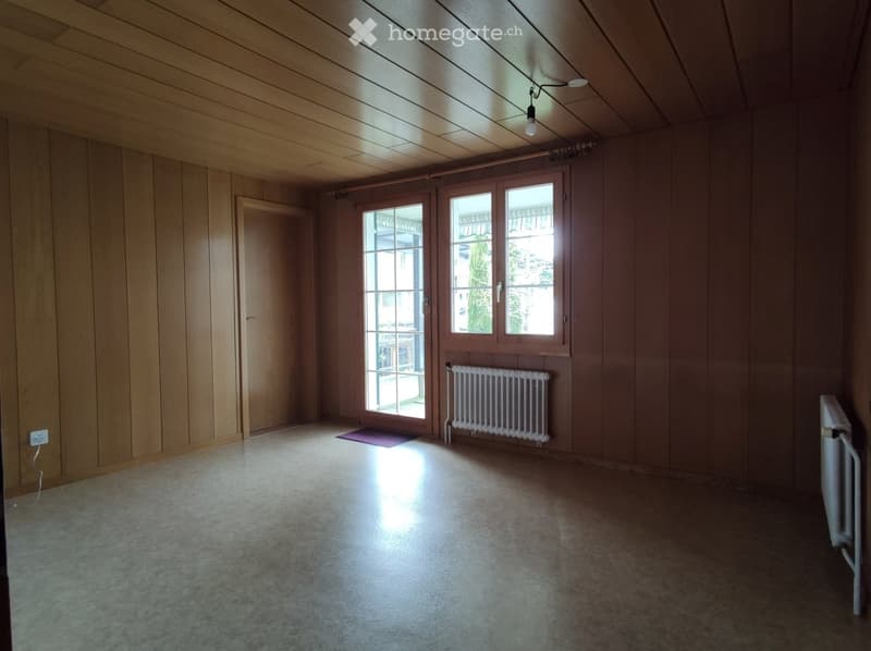 Empty room with wooden walls and ceiling, large windows, and a radiator. No furniture or equipment present.