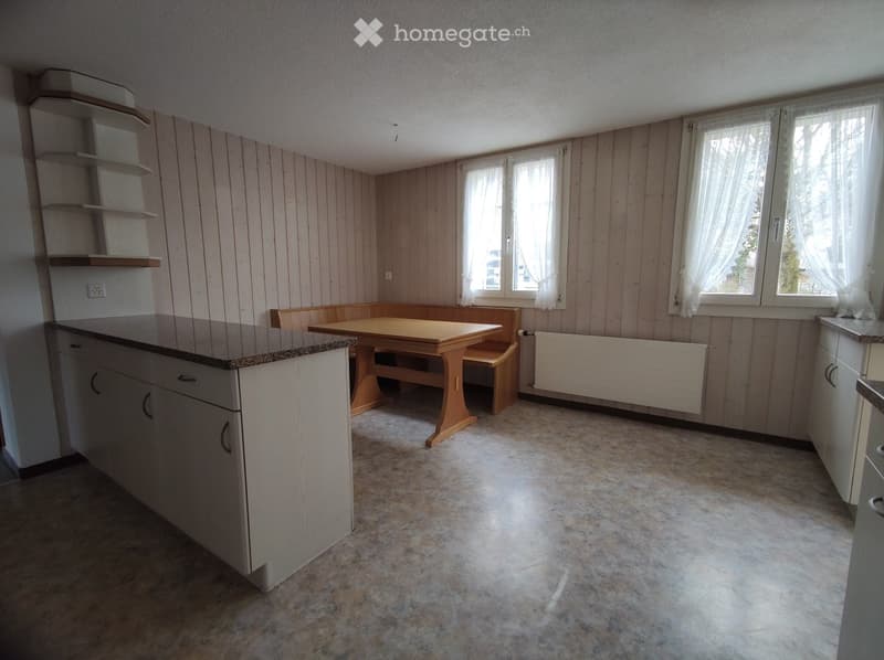 Kitchen with wooden panel walls, granite countertop, white cabinets, and a small dining area with a table and bench.