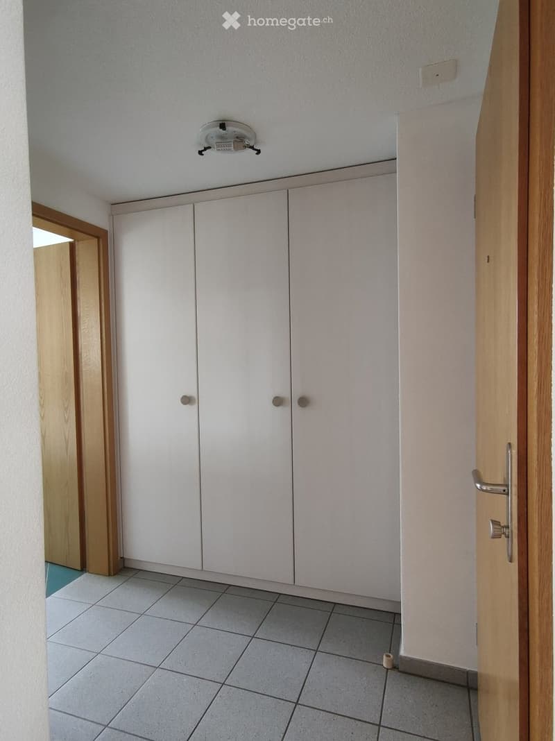 Empty room with white built-in cabinets, tiled floor, and a partially open wooden door leading to another space.