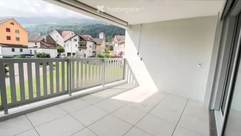 Balcony with white tiled floor, grey railing, and scenic view of a town and mountains.