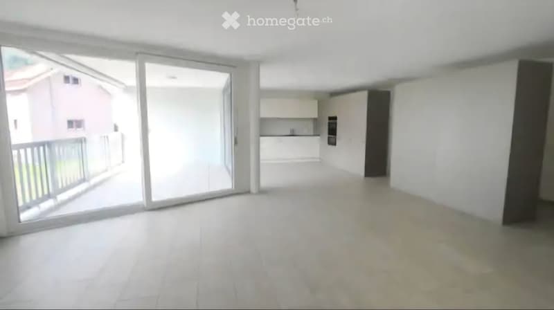 Empty living space with white walls, large sliding glass doors leading to a balcony, and a view of a neighboring building.