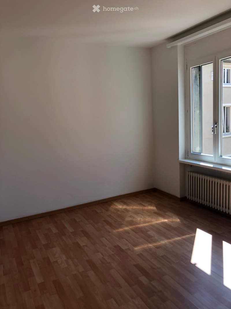 Empty room with wooden flooring and white walls, featuring a window with a radiator below it.