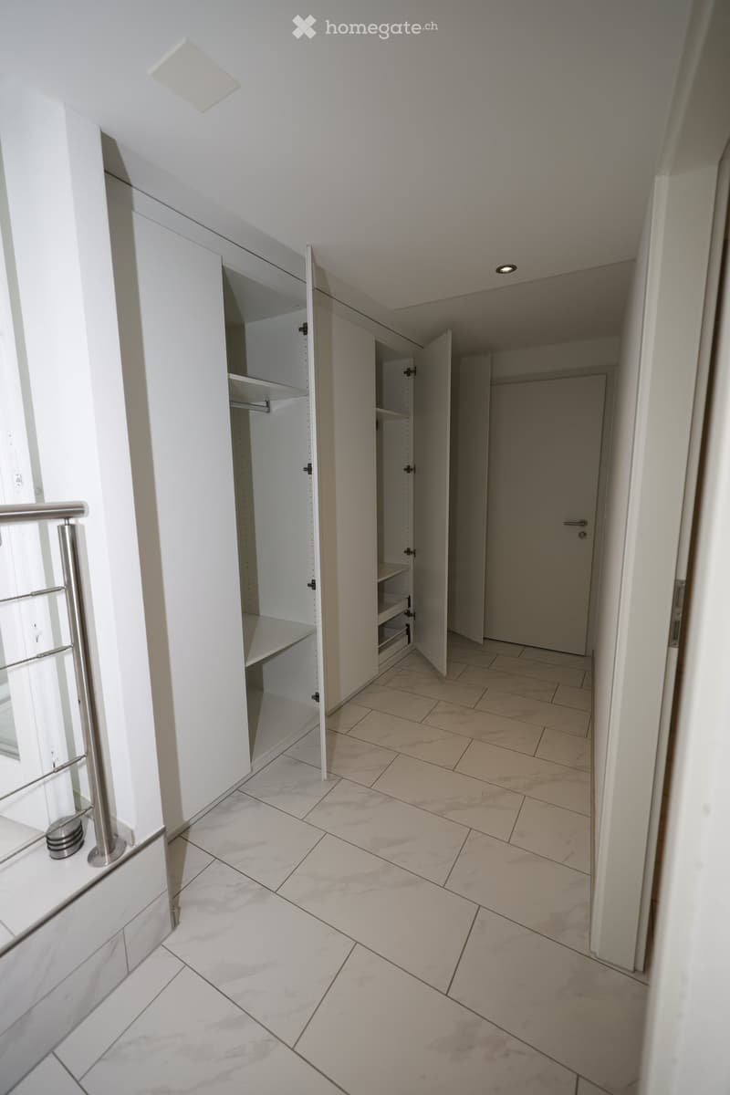 Empty hallway with white walls, marble flooring, built-in white closet with shelves, and a closed door at the end.