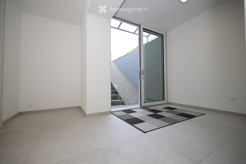 Empty room with white walls, tiled floor, and a checkered rug near a sliding glass door leading to a staircase.