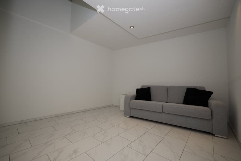 A modern living room with a grey sofa, two black pillows, and a marble tiled floor.