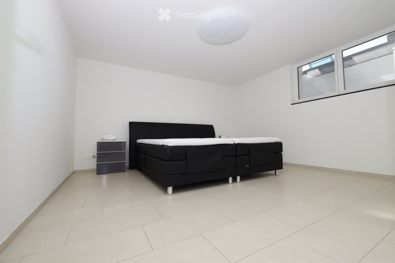 Modern bedroom with a black bed, white bedding, a nightstand with a lamp, and large windows with blinds.