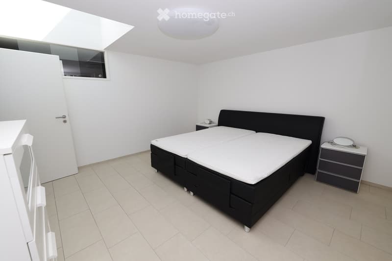 Modern bedroom with a black bed frame, white mattress, nightstand, and a mirror on the wall.