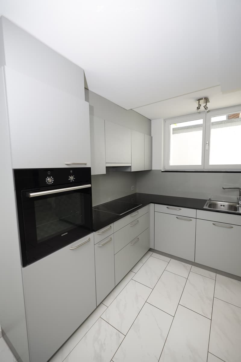 Modern kitchen with white cabinets, black countertop, and stainless steel appliances including an oven and sink.