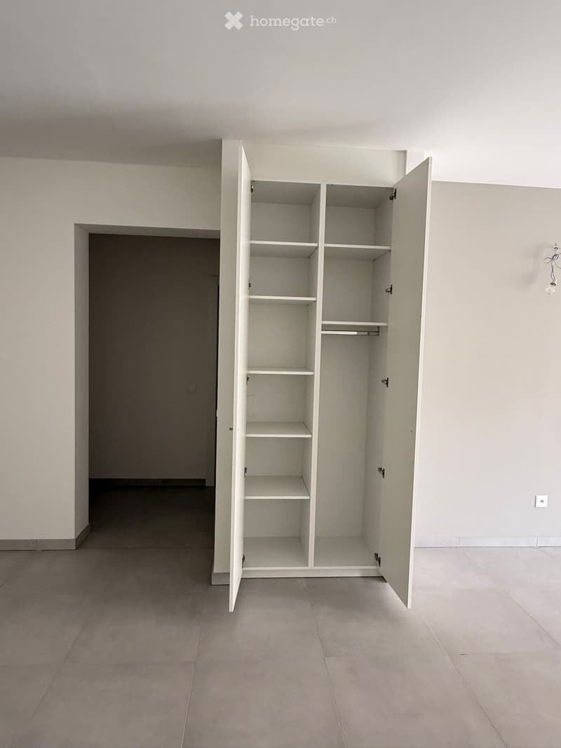 Empty room with light-colored walls, tiled floor, and an open built-in closet with multiple shelves and a hanging rod.