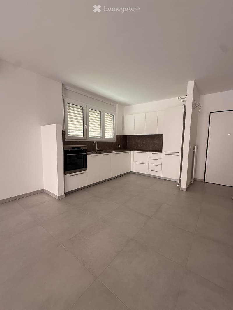 Empty kitchen with white cabinets, stainless steel oven, sink, and tiled floor.
