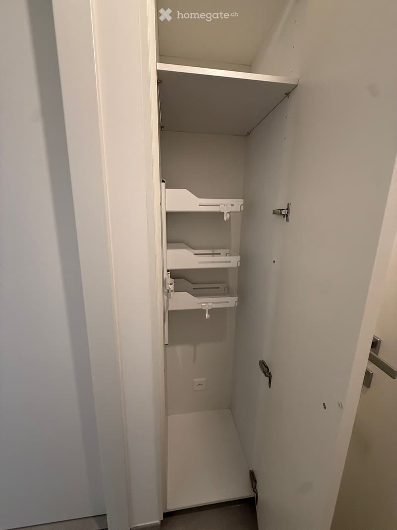 Empty closet with white shelves and a small electrical outlet on the wall.
