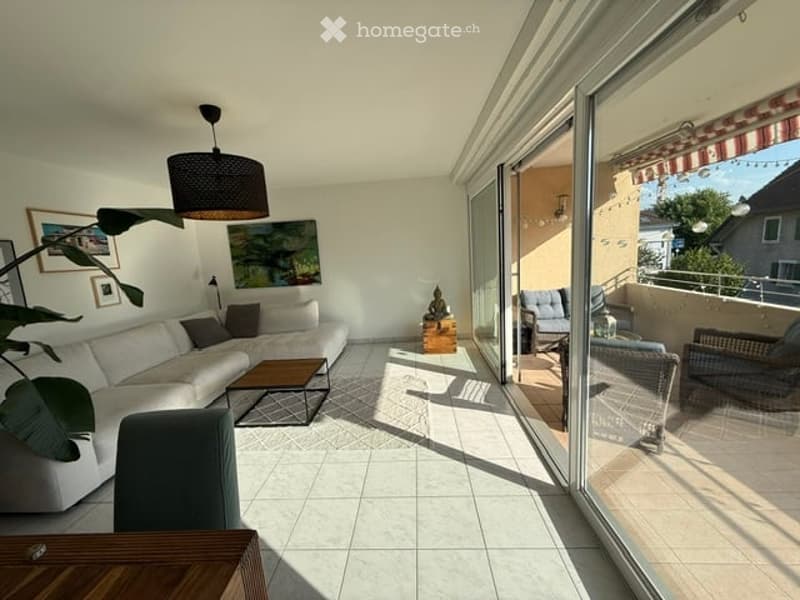 Bright living room with large sliding glass doors opening to a balcony, white sofa, coffee table, floor lamp, and artwork on the walls.
