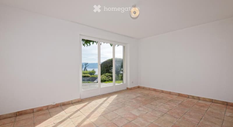 Empty room with white walls, tiled floor, large sliding glass doors leading to an outdoor area with a scenic view.