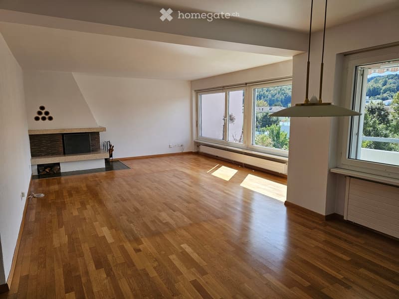 Empty room with wooden flooring, large windows, and a fireplace. No furniture or equipment present.