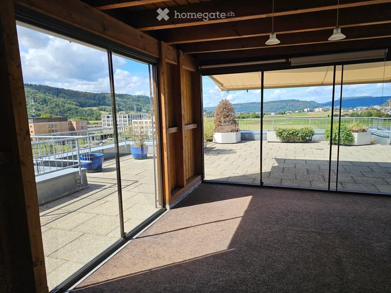 Bright, open space with large glass doors leading to a balcony area, featuring a scenic view of a valley and mountains.