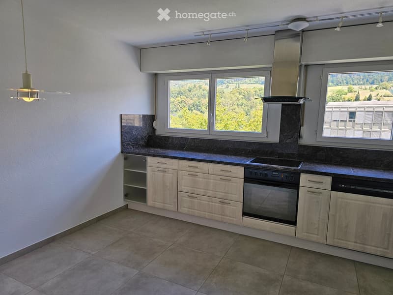 Modern kitchen with light wood cabinets, stainless steel appliances, and large windows offering a scenic view.