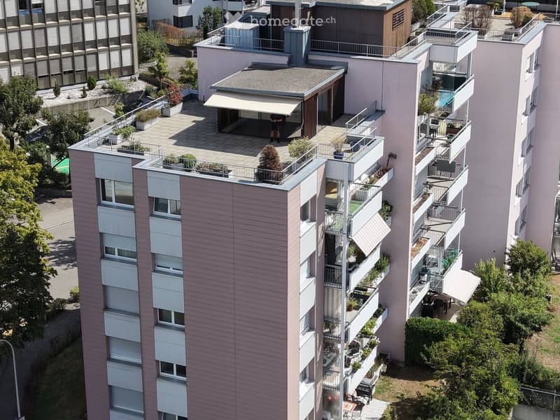Aerial view of a modern multi-story residential building with multiple balconies, greenery, and outdoor seating areas.