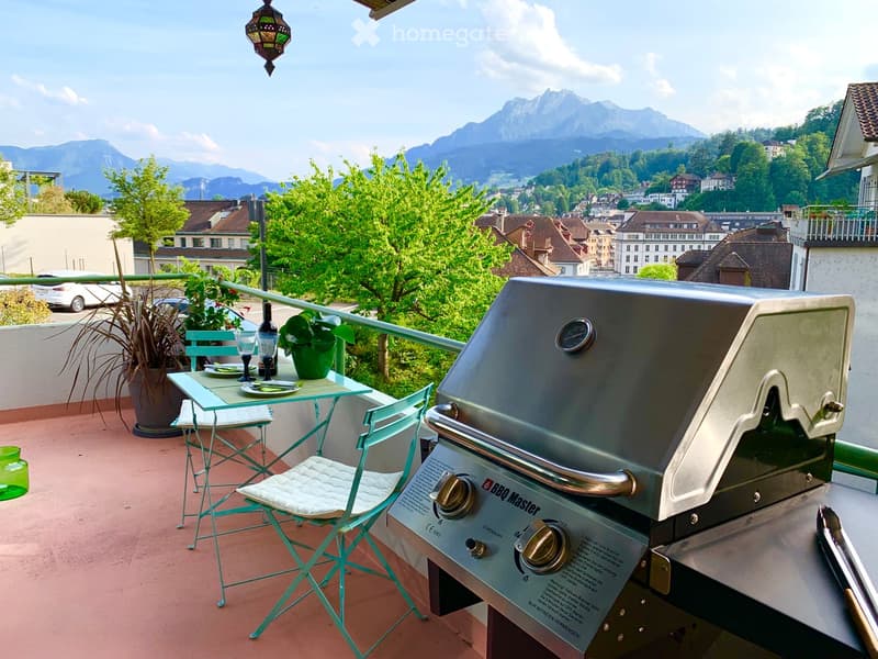 Balcony with a grill, table, chairs, and a scenic mountain view.