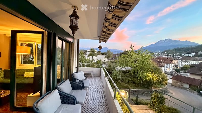 Balcony with wicker chairs, small table, and scenic mountain view.