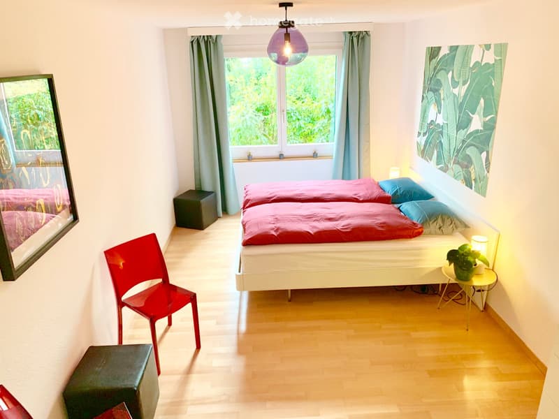 Cozy bedroom with two single beds, red bedding, a red chair, a small table with a plant, and a mirror on the wall.
