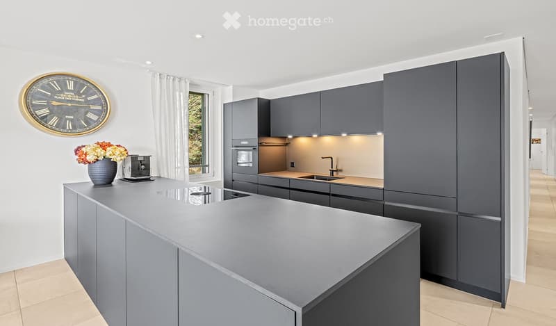 Modern kitchen with grey cabinetry, a central island, built-in appliances, and a decorative clock on the wall.