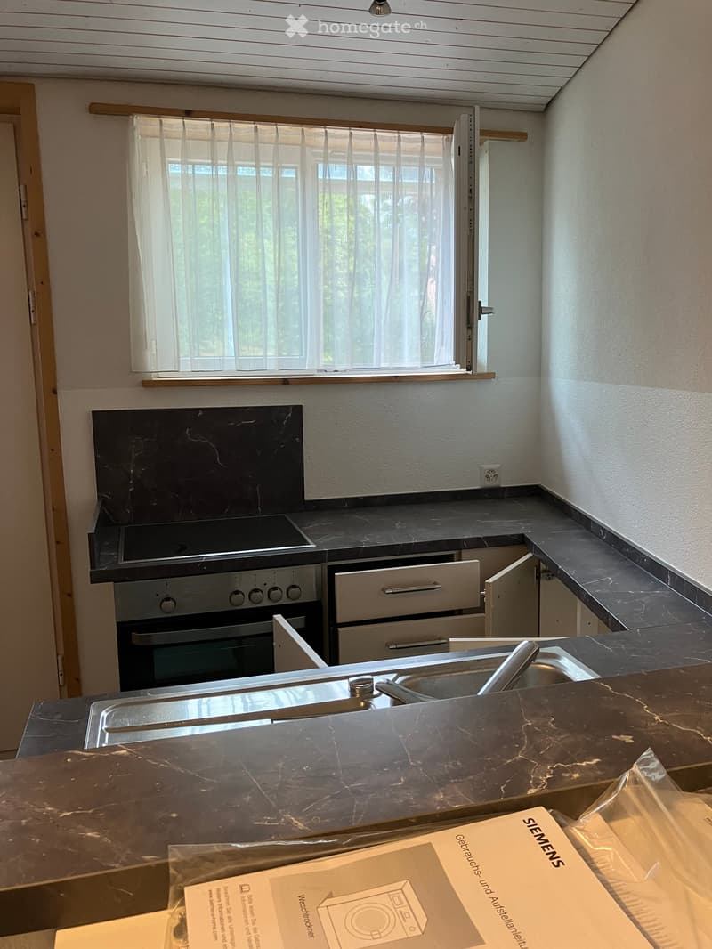 Modern kitchen with black marble countertops, stainless steel sink, and built-in oven. Window with blinds provides natural light.