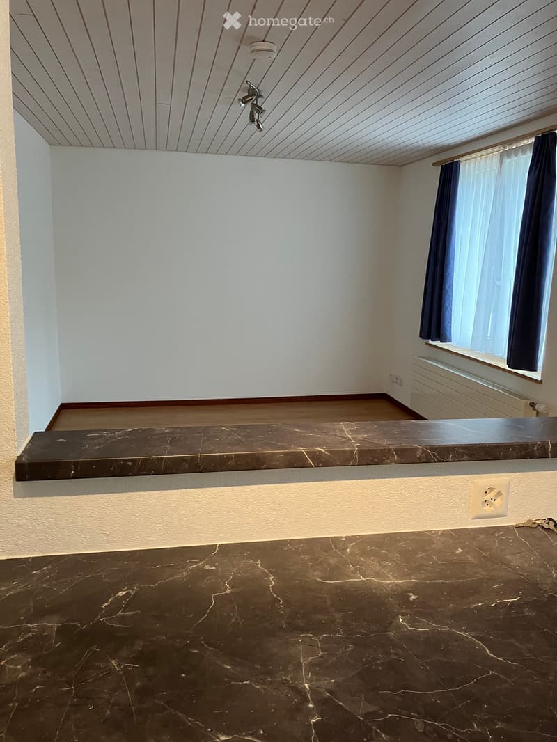 Empty room with marble flooring, white walls, and a window with dark curtains. Features a built-in shelf and a ceiling light fixture.