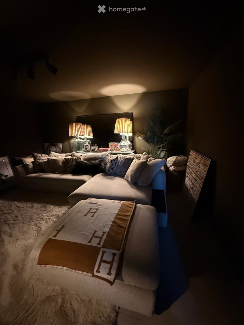Cozy living room with a sectional sofa, throw blanket, coffee table with lamps, picture frame, and a plant in the corner.