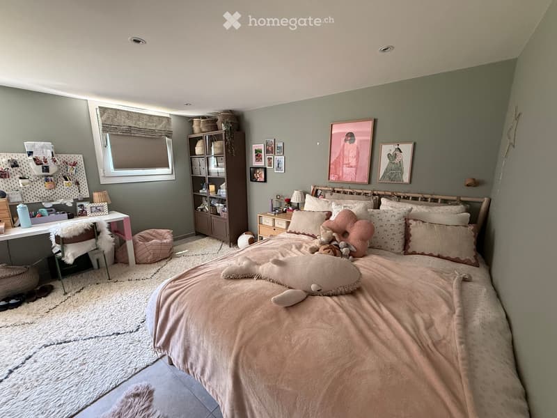 Cozy bedroom with a large bed, nightstand, lamp, and various decorative items including framed pictures and toys.