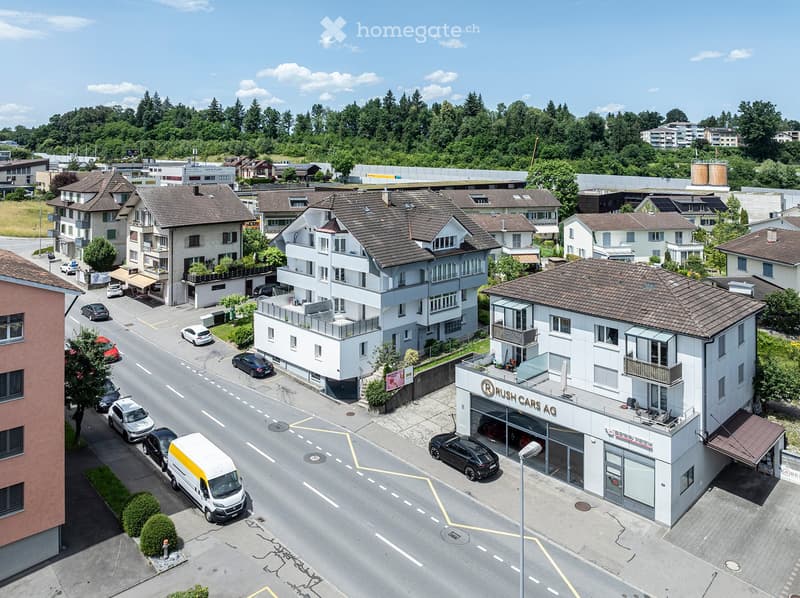 Aerial view of a residential area with multiple multi-story houses, a car dealership, and surrounding greenery.