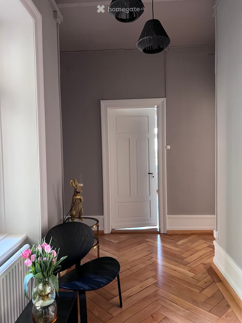 wooden floor, gray walls, white door, black chair, glass table, pink flowers, radiator