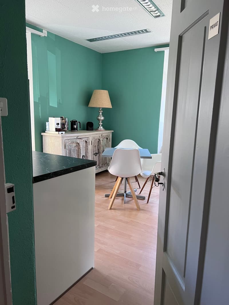 Dining area with wooden floor, green walls, a table with chairs, a cabinet with a lamp, a coffee machine, and a kettle.