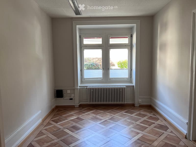 Empty room with wooden herringbone flooring, white walls, large window with double glazing, radiator, and electrical outlets.
