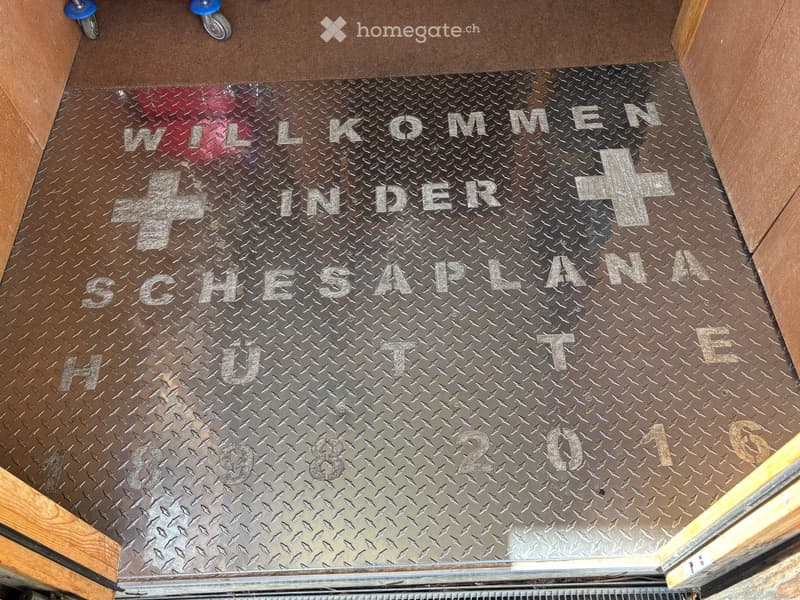 Metal floor with engraved text "WILLKOMMEN IN DER SCHESAPLANA HÜTE1898-2014" and decorative crosses.