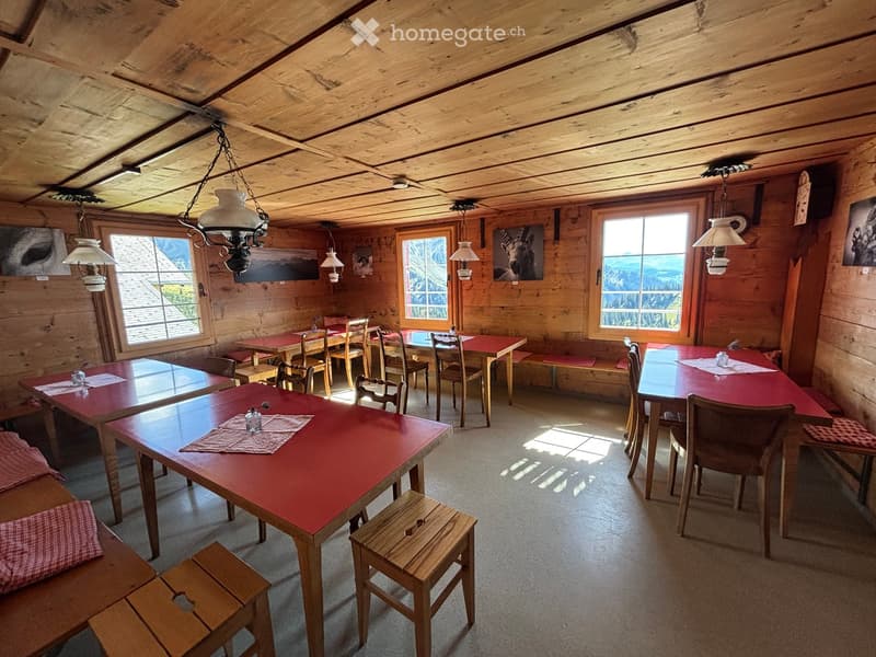 Cozy wooden-paneled dining area with multiple red tables and wooden chairs, wooden stools, benches, and hanging lamps.