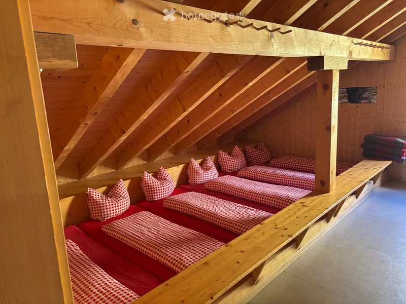 Cozy attic room with wooden beams and slanted ceilings, featuring built-in wooden bed platforms with red and white checkered bedding and pillows.
