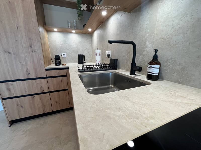 Modern kitchen with a marble countertop, stainless steel sink, black faucet, and wooden cabinets.