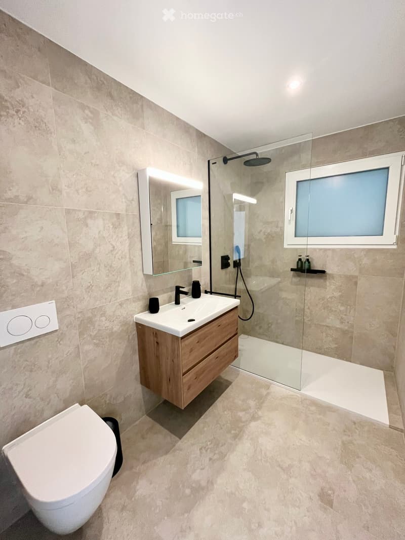 Bathroom. Modern bathroom with beige tiles, a white toilet, a wooden vanity with a sink, a large mirror, and a glass-enclosed shower with a modern showerhead.