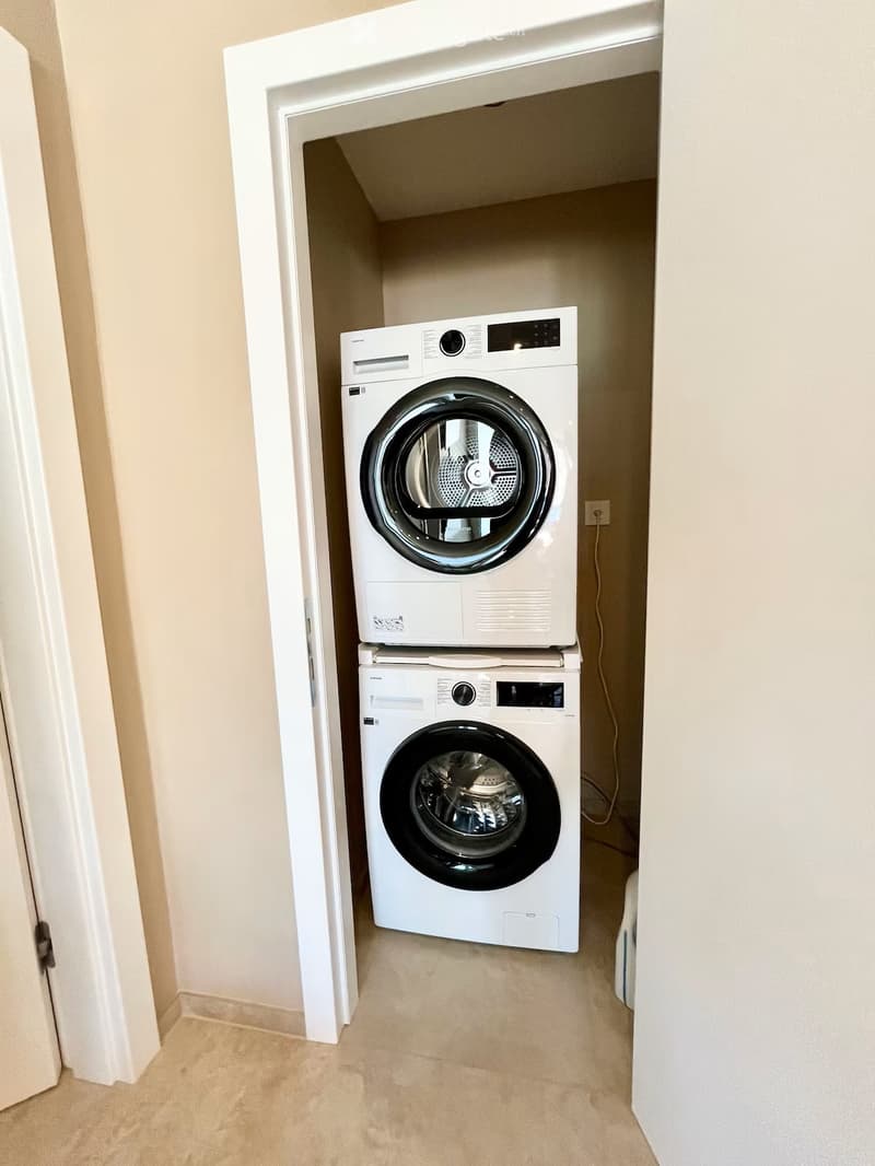 Bathroom. A small, well-lit laundry area with a stacked washer and dryer unit against the wall.