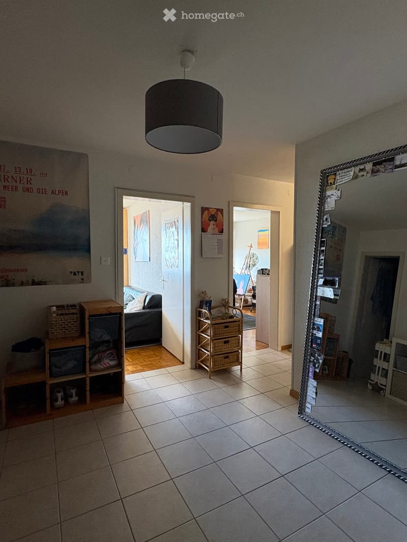Hallway with tiled floor, pendant light fixture, open doors leading to adjacent rooms, visible furniture in adjacent spaces.