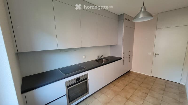Modern kitchen with white cabinets, black countertops, a sink, a faucet, and an oven. The space is clean and well-lit with a hanging light fixture.